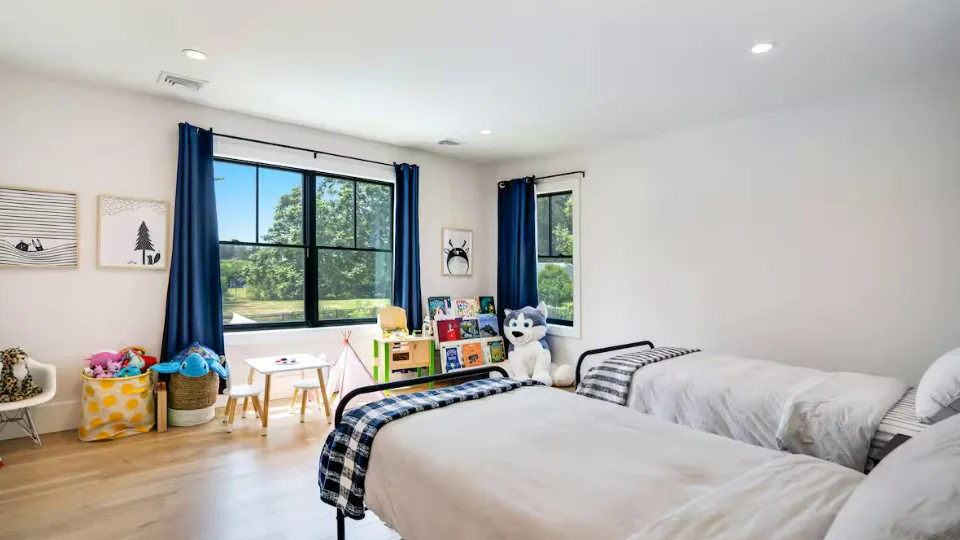 Un dormitorio luminoso con dos camas, una ventana grande y juguetes infantiles.