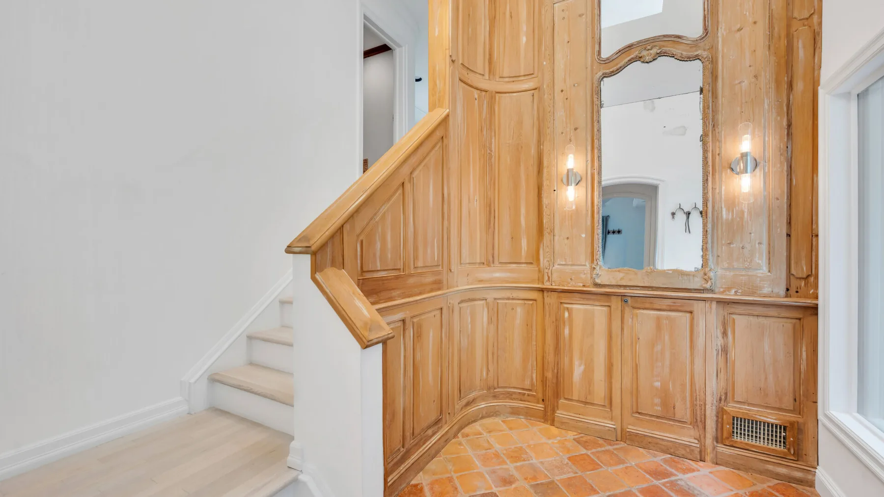 Un descansillo interior tiene una barandilla de madera, paredes con paneles y un espejo.