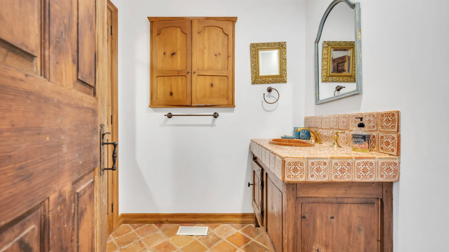 Un lavabo de baño con azulejos está bajo un espejo junto a gabinetes de madera.