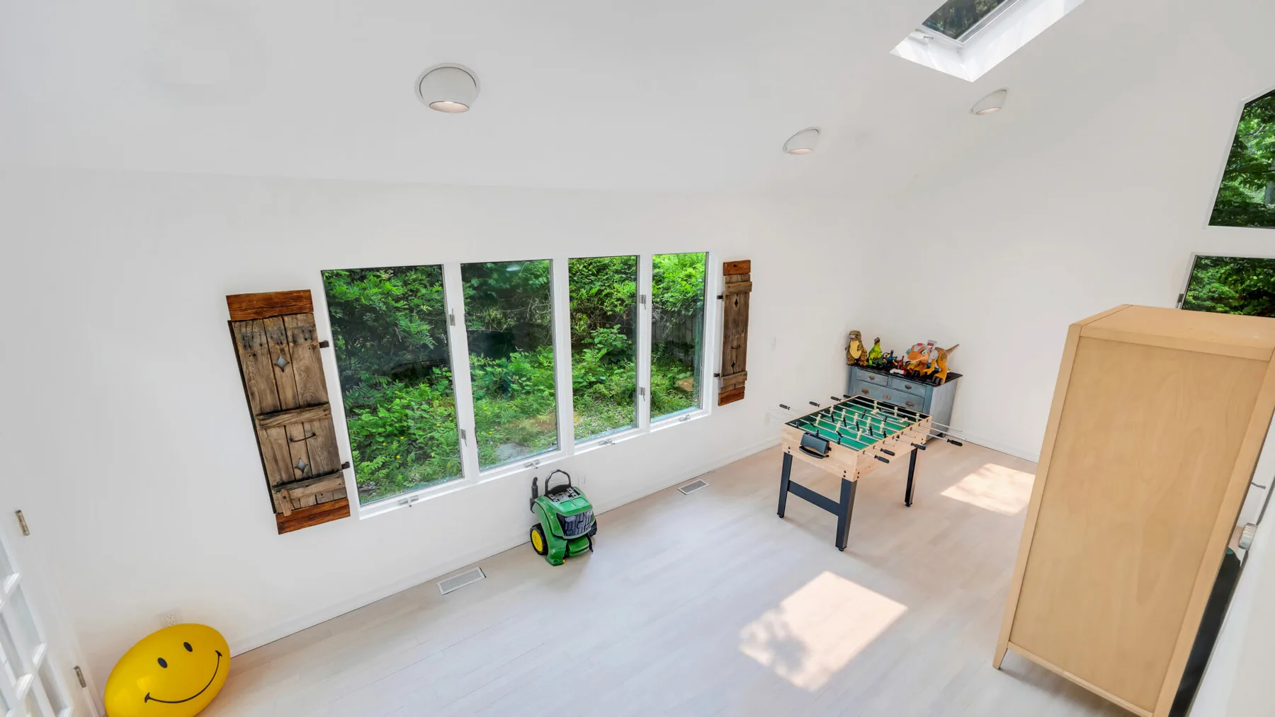 Una luminosa sala de juegos con futbolín y grandes ventanas con vistas a la vegetación.