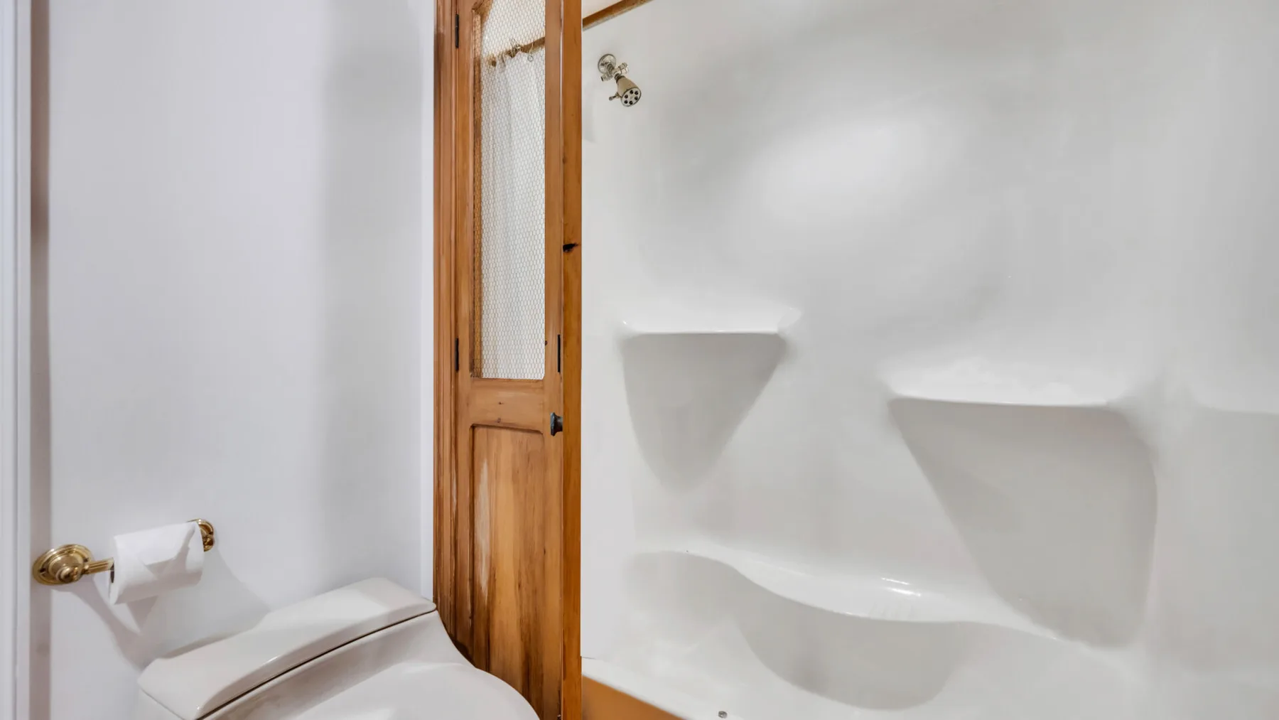 Un baño blanco con inodoro, nichos en la pared y una puerta de madera.