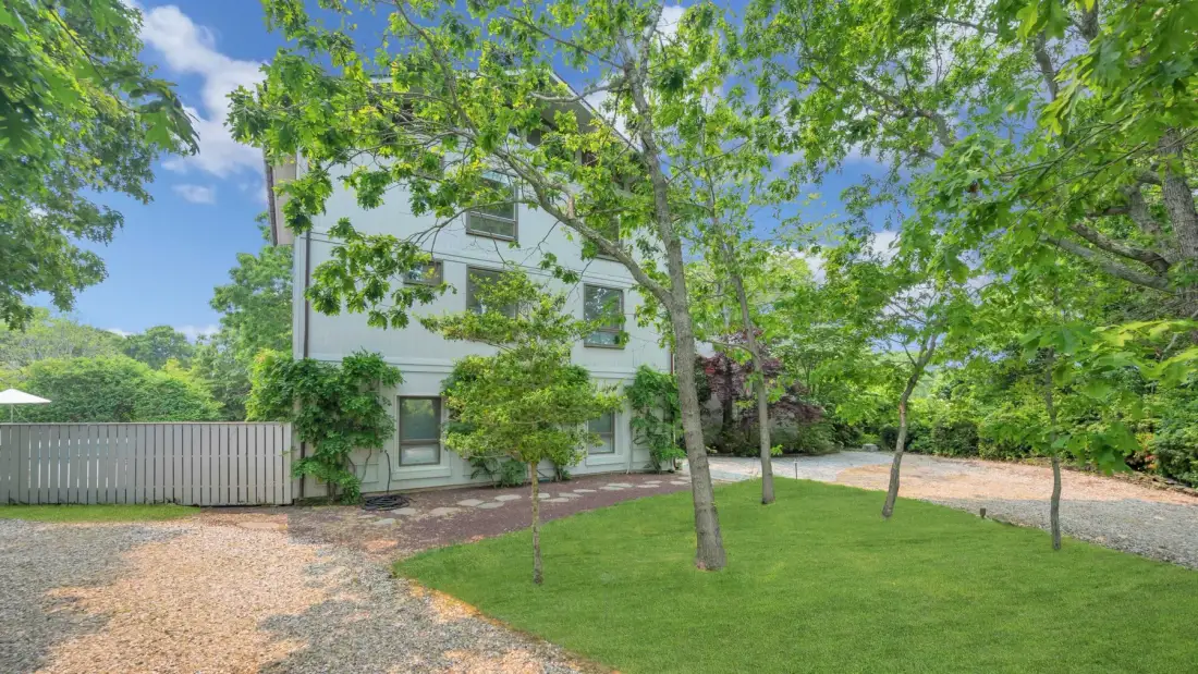 Una casa blanca se alza detrás de un césped verde y árboles frondosos.