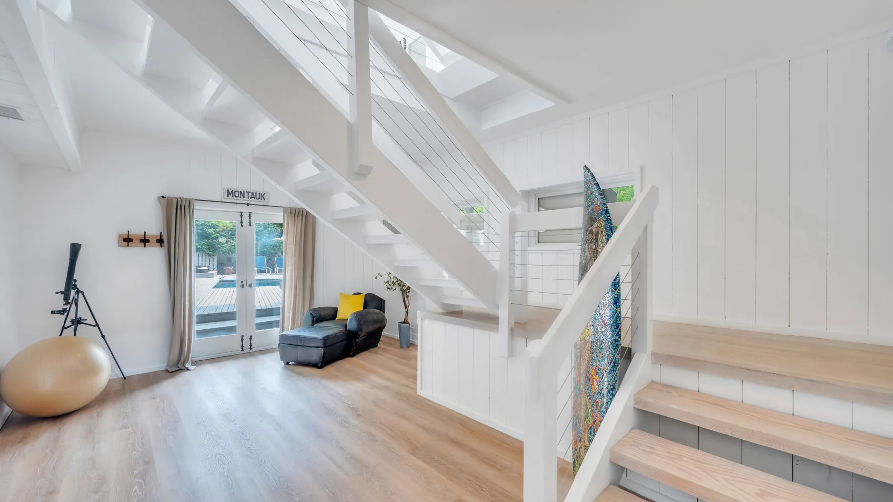 Una luminosa sala bajo una escalera, con asientos junto a puertas de vidrio.