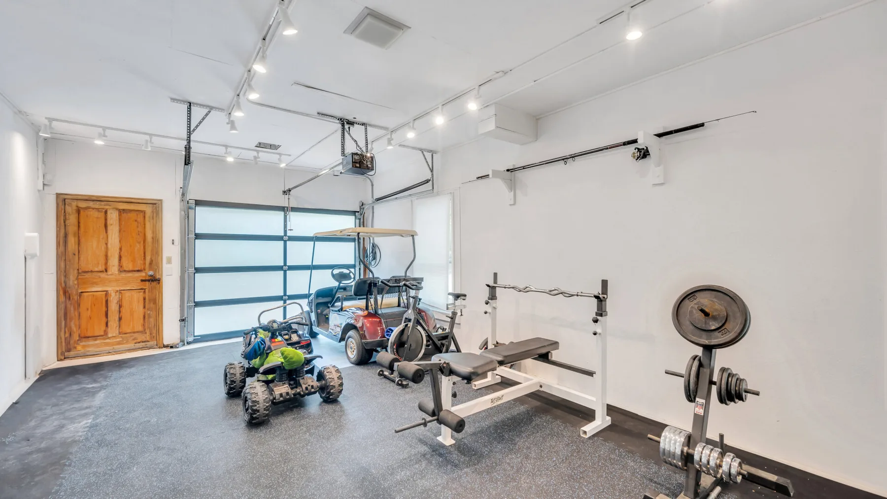 Un gimnasio luminoso en un garaje con equipo de ejercicio y una puerta de madera.
