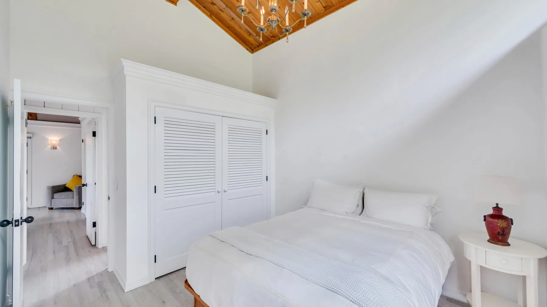 Un dormitorio luminoso con una cama blanca, un armario y una mesita de noche.