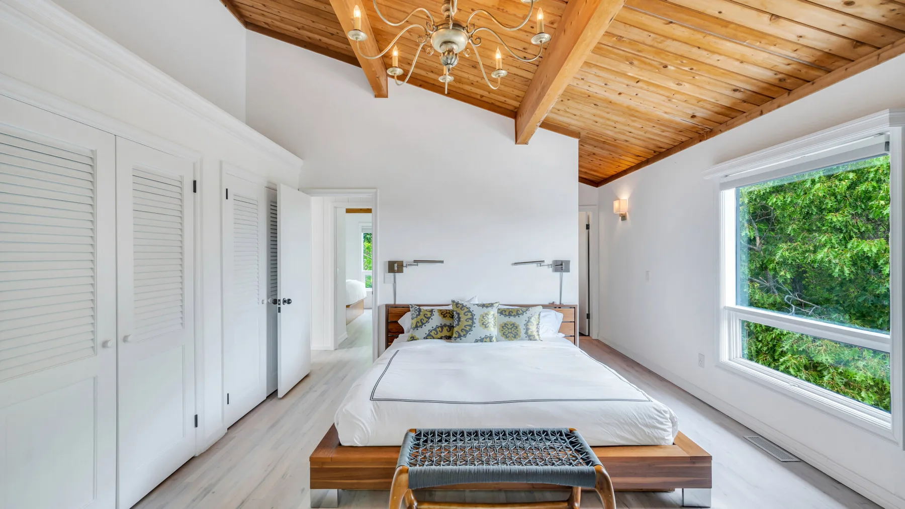 Un dormitorio luminoso con una cama grande bajo un techo de madera abovedado.