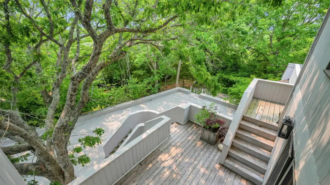 Una terraza de madera y unas escaleras dan a una zona exterior rodeada de árboles.