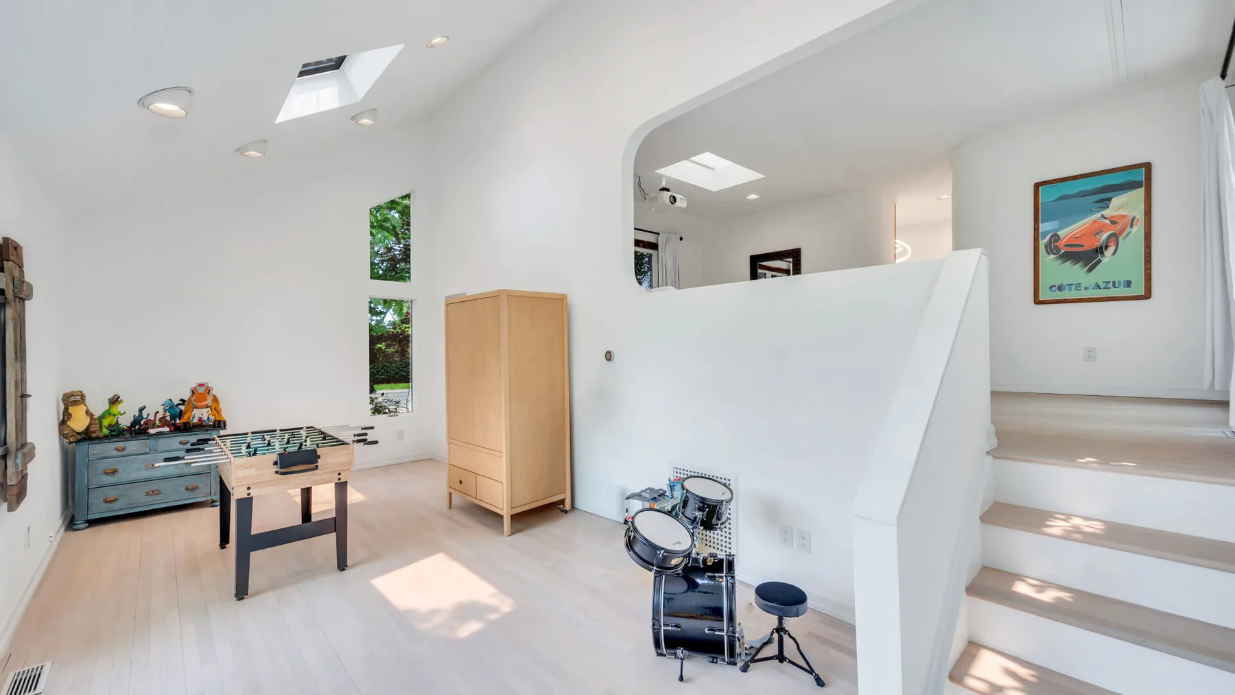 Una habitación luminosa tipo loft con una batería junto a una escalera y arte enmarcado.