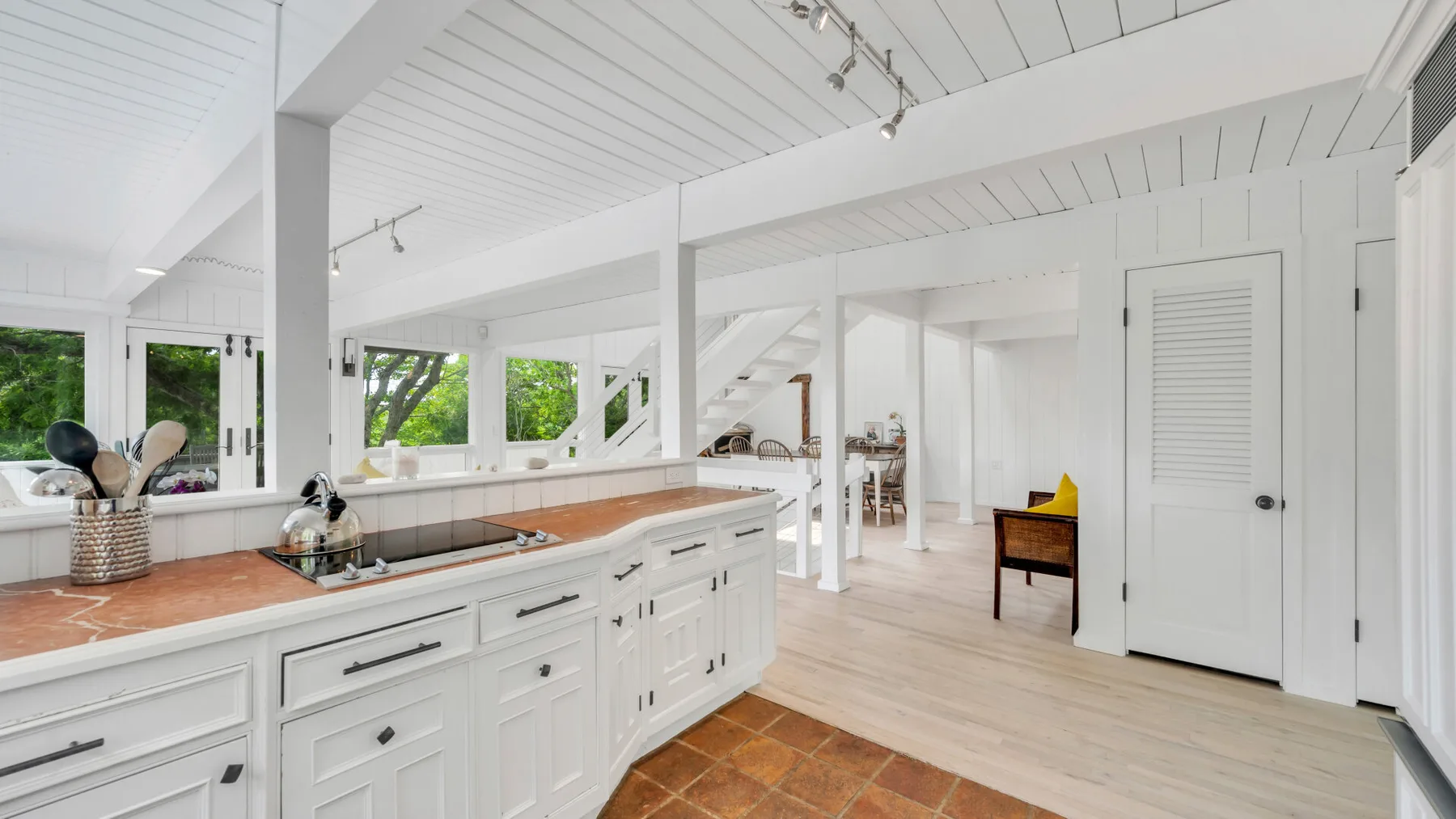 Una cocina blanca y luminosa con una isla larga y un comedor abierto.
