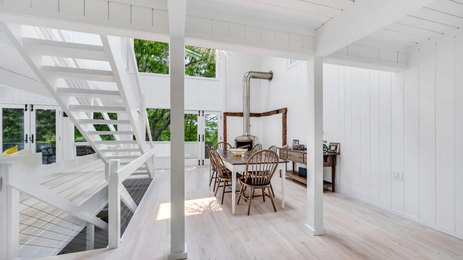 Una estancia luminosa y diáfana con una mesa de comedor bajo una escalera blanca.