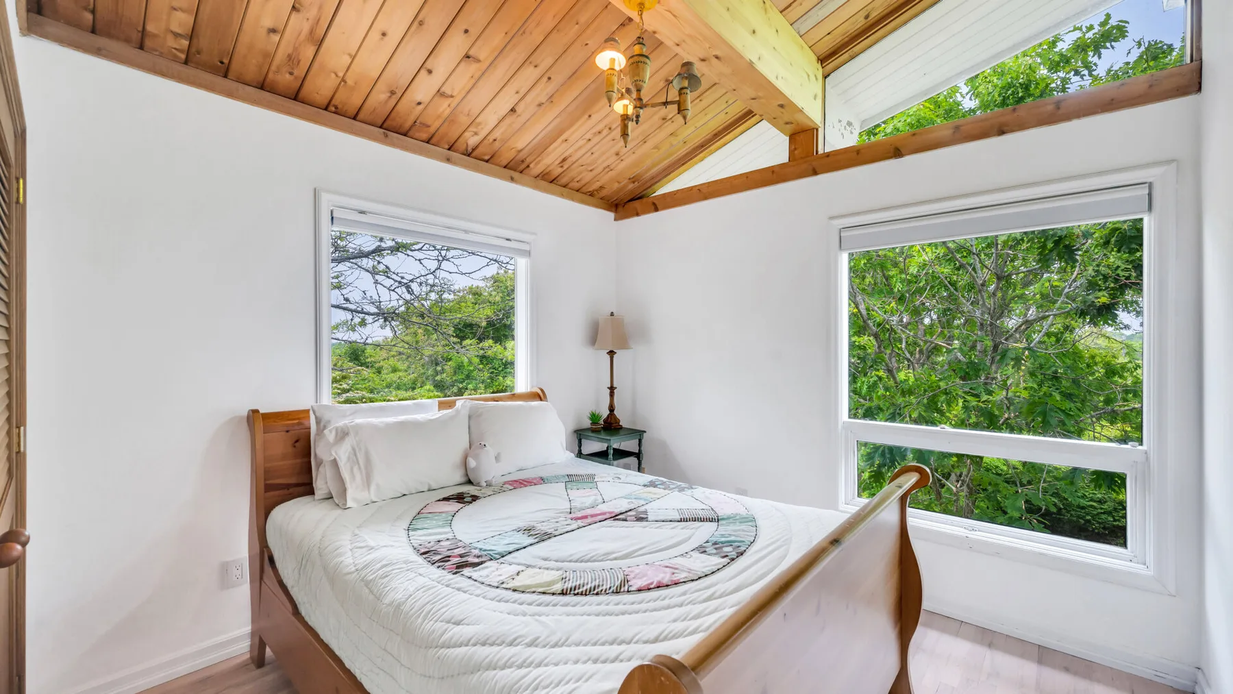 Un dormitorio con una cama bajo un techo inclinado de madera y ventanas grandes.
