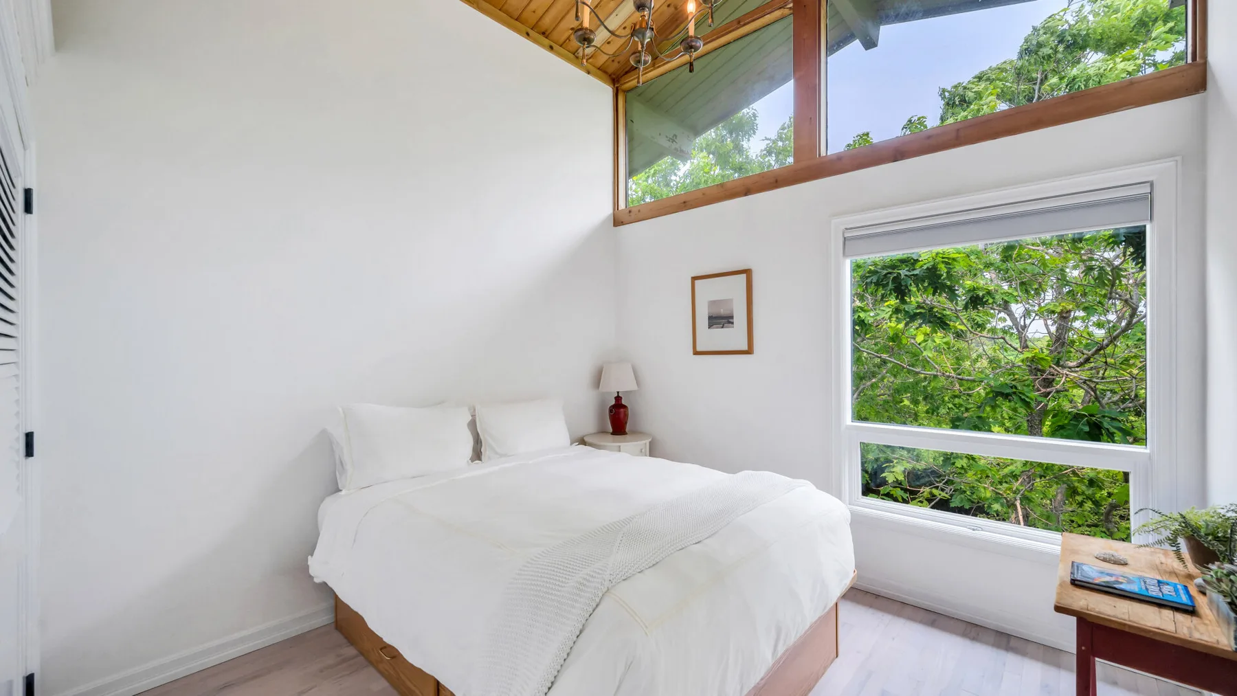 Un dormitorio luminoso con una cama junto a grandes ventanas con vistas a la vegetación.