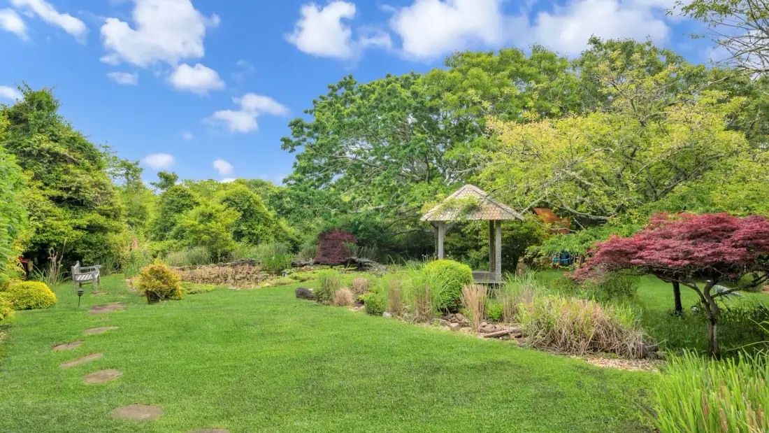 Un jardín cuidado con césped, arbustos floridos y un pequeño cenador de madera.