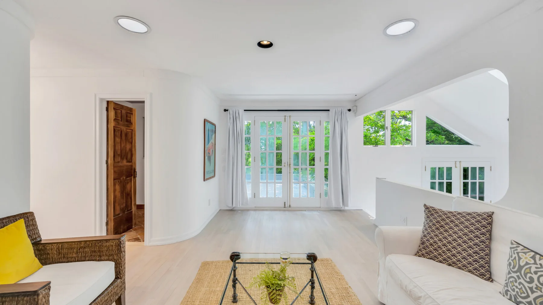 Una sala luminosa con asientos alrededor de una mesa de centro de vidrio y puertas al patio.
