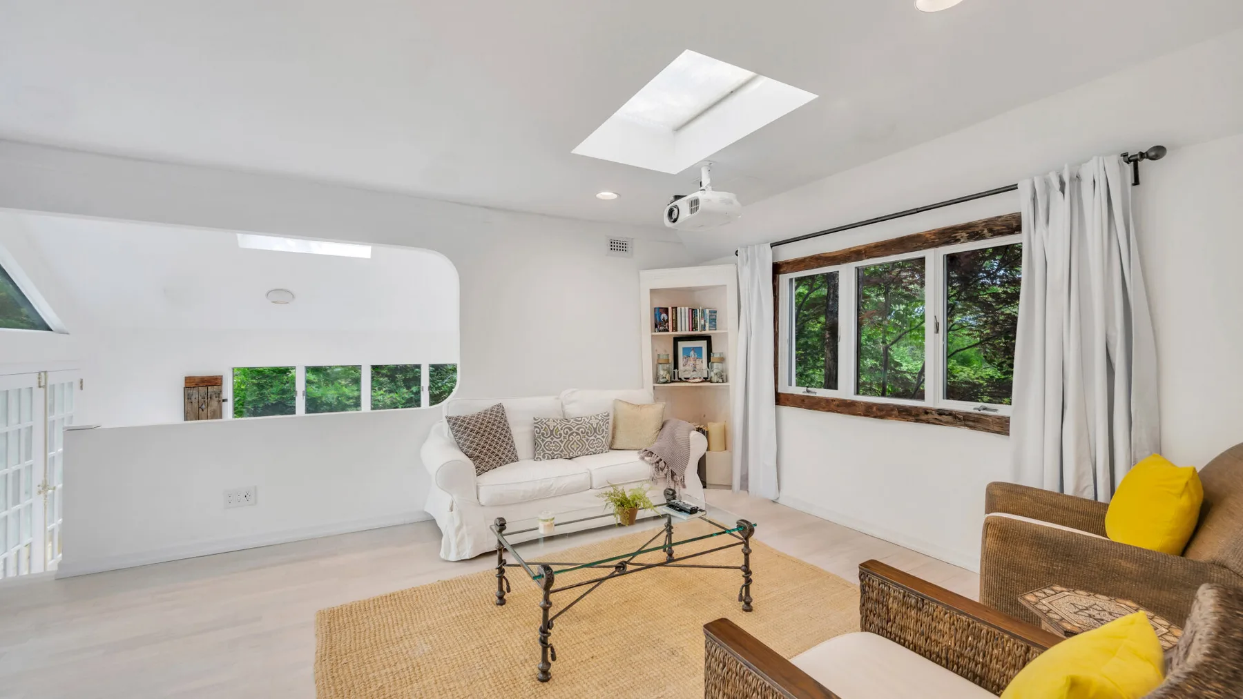Una sala luminosa con asientos, una mesa de centro de vidrio y ventanas con vistas a la vegetación.