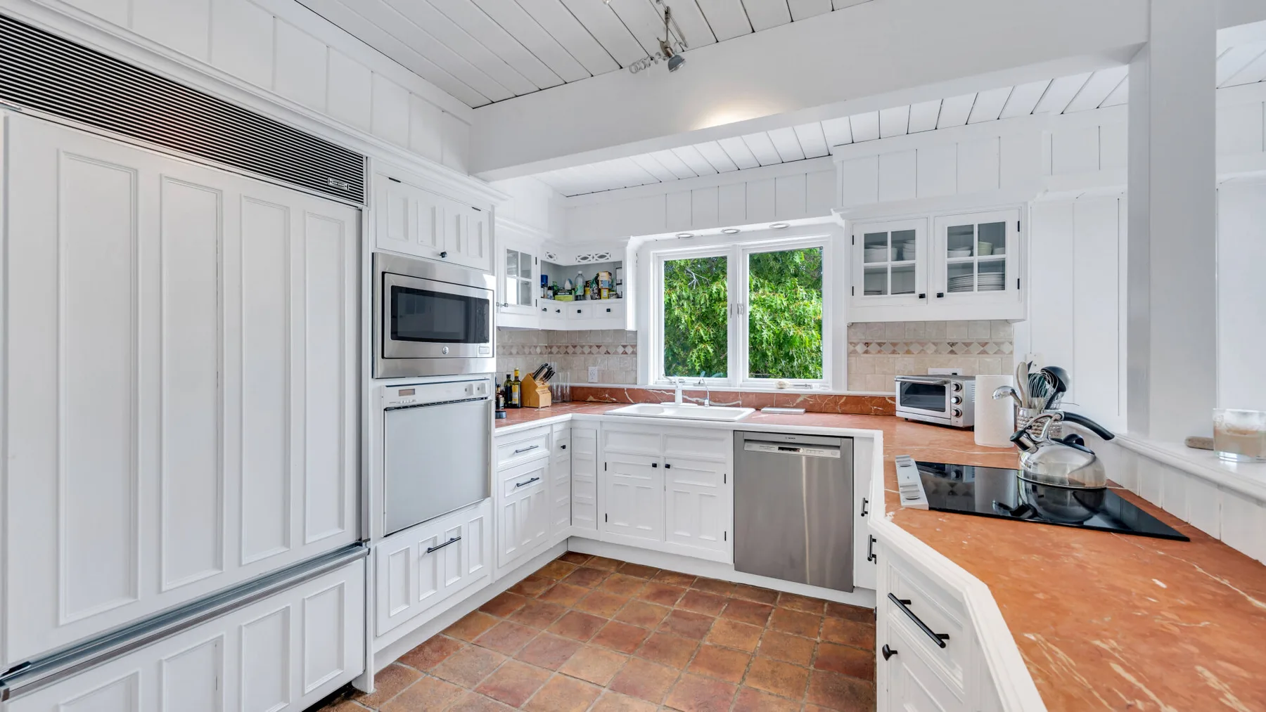 Una cocina blanca y luminosa con una ventana central y encimeras de tono madera.