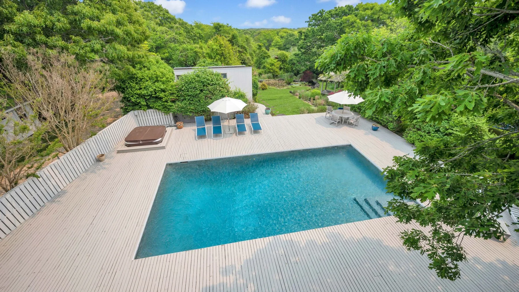 Una piscina al aire libre está rodeada por una amplia terraza y árboles verdes.