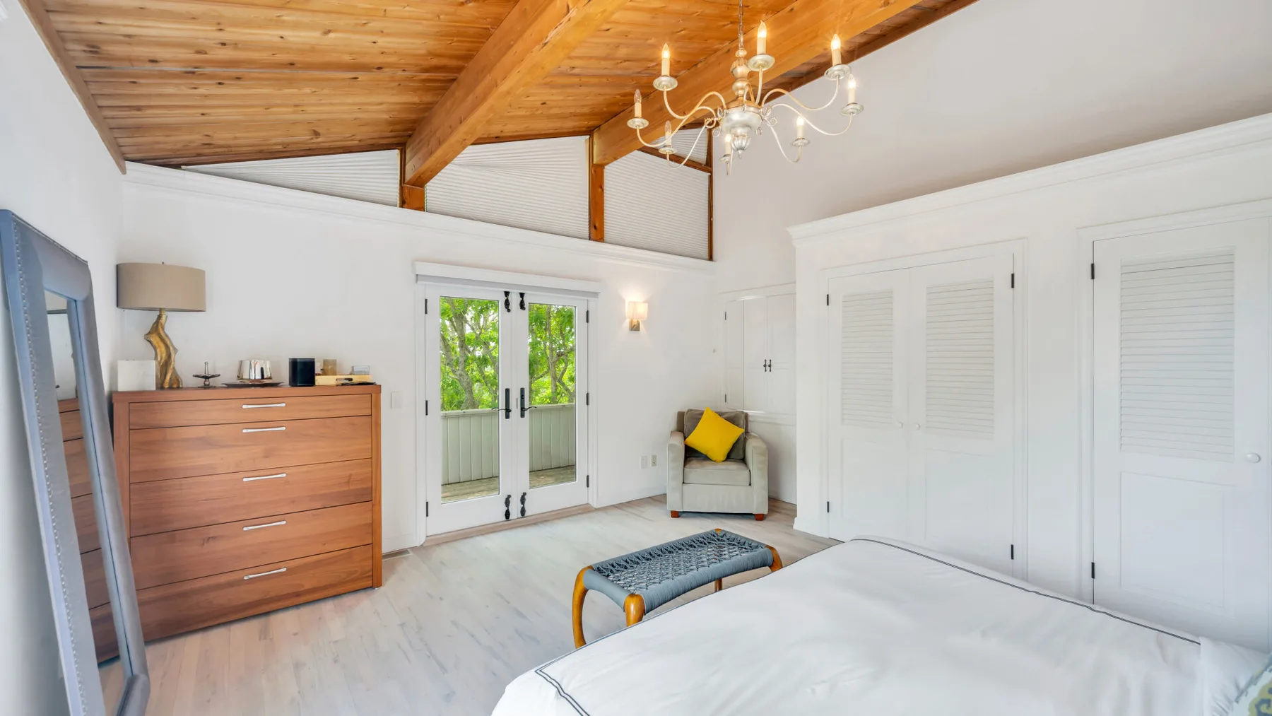 Un dormitorio luminoso con una cama, una cómoda de madera y puertas de vidrio que dan a un balcón.