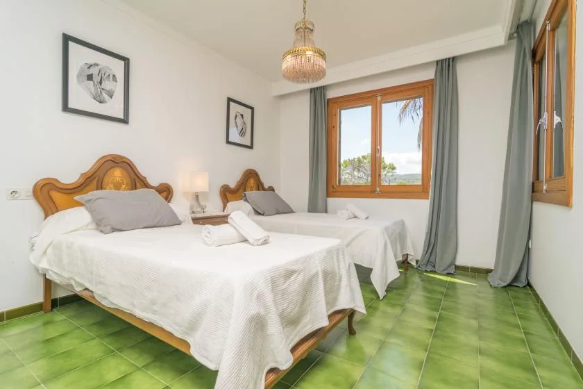 Un dormitorio con dos camas, ropa de cama blanca y una ventana con vistas a la vegetación.