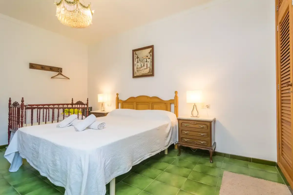 Un dormitorio con una cama, mesitas de noche y suelo de baldosas verdes.