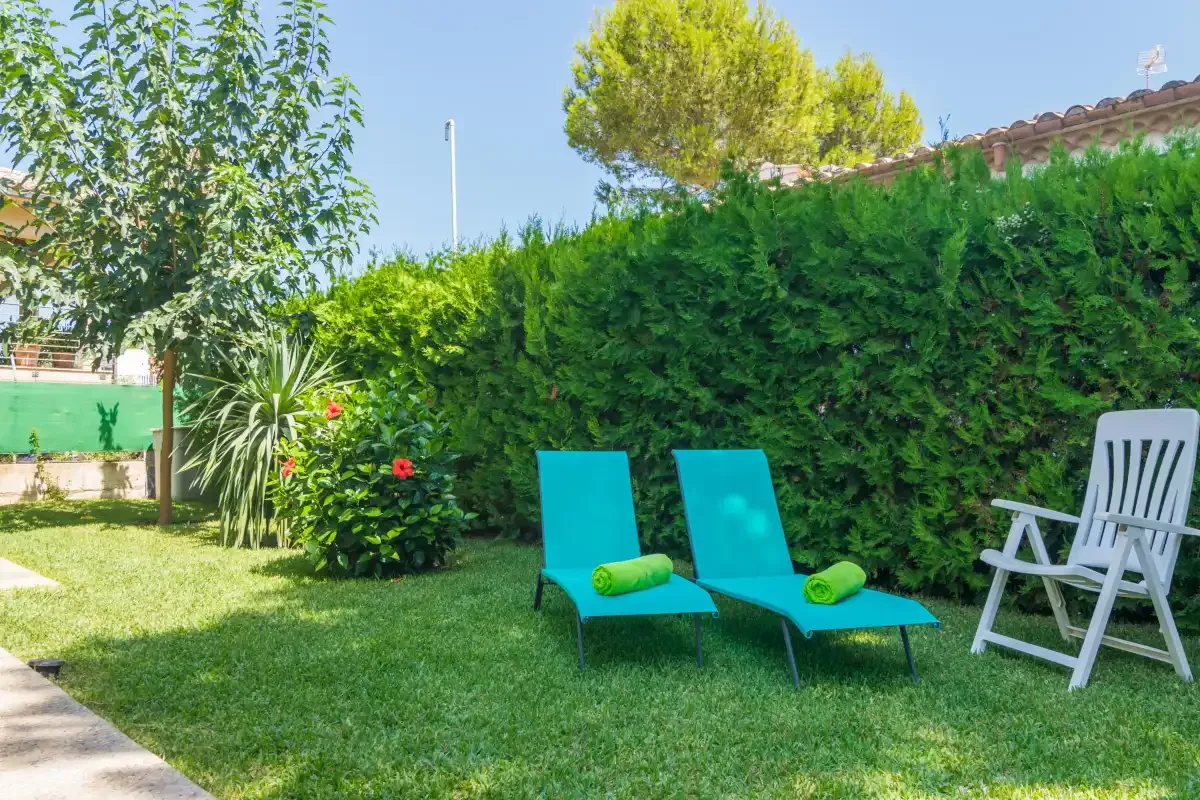Una zona de descanso en el jardín con dos tumbonas turquesas junto a un seto alto.