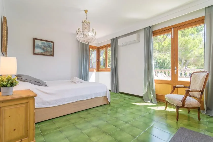 Dormitorio con una cama grande, suelo de baldosas verdes y puertas que dan a un balcón.