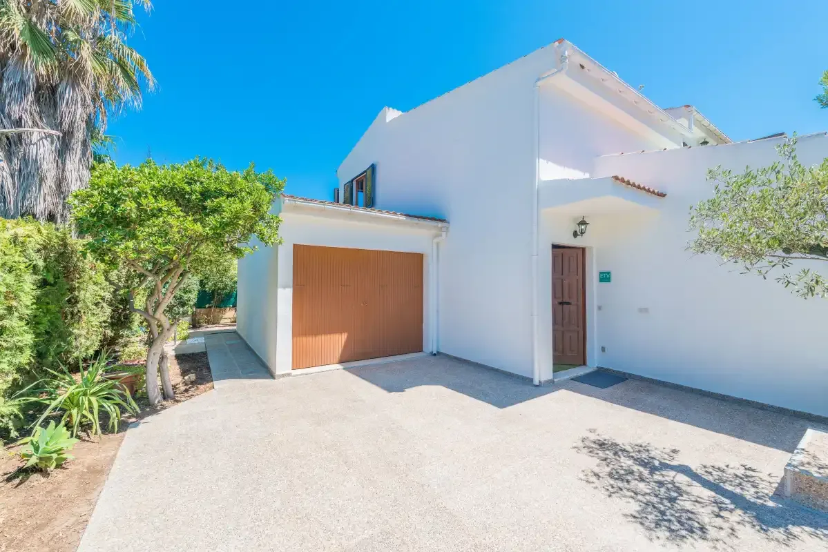 Exterior de una casa blanca con puerta de garaje y entrada pavimentada.