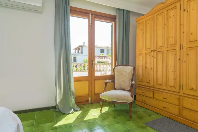 Un rincón de dormitorio con una silla junto a una ventana y un armario grande de madera.