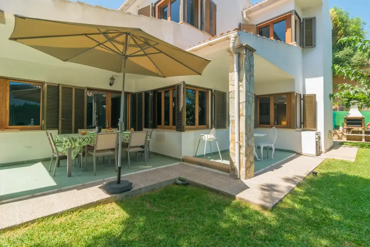 Patio de una casa con asientos al aire libre y una sombrilla grande junto al césped.