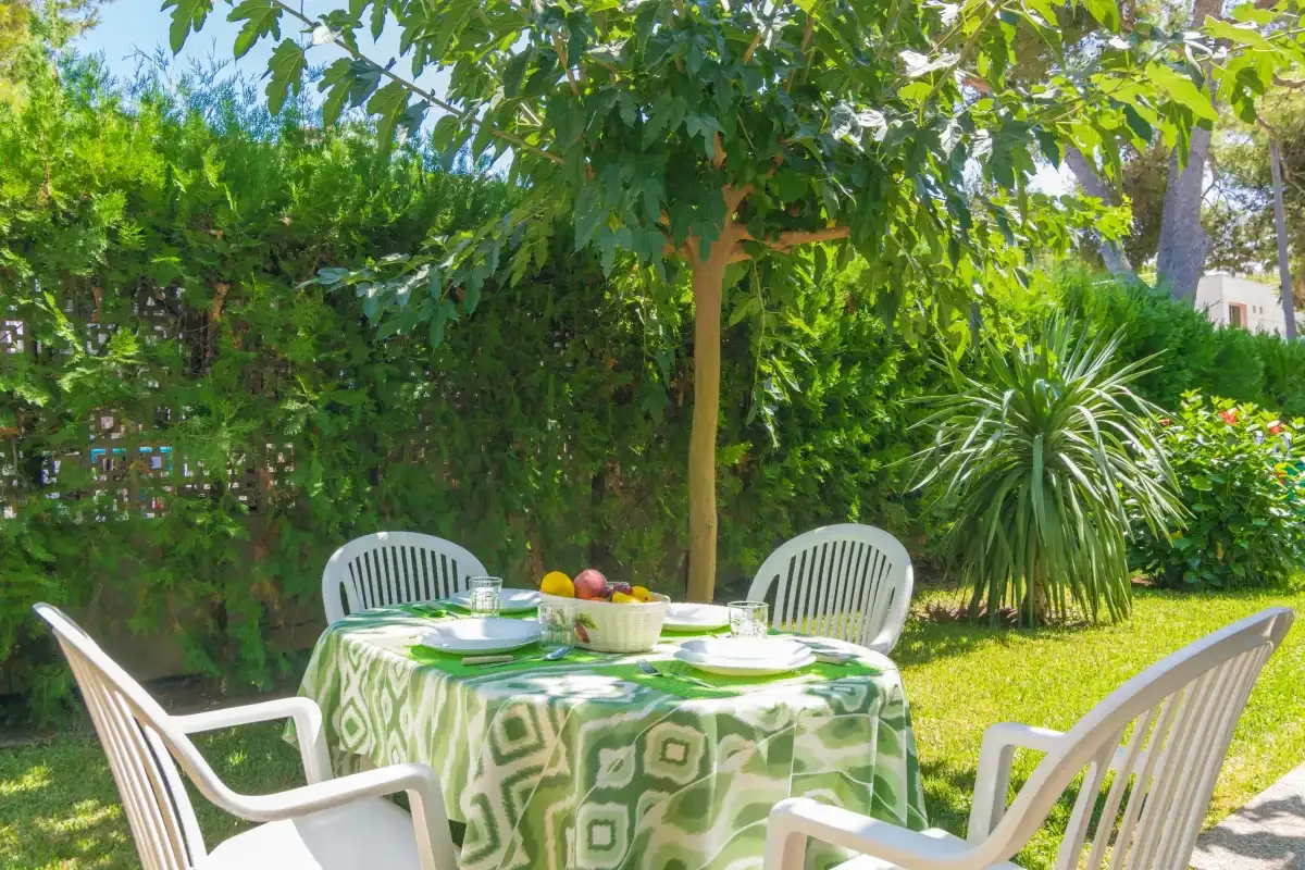 Una zona de comedor en el jardín con una mesa bajo árboles frondosos.