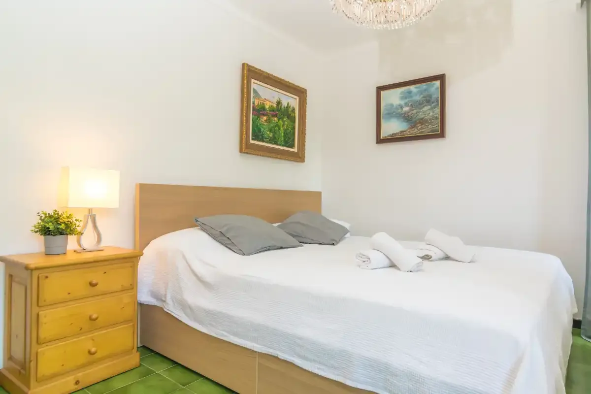 Un dormitorio con una cama bien tendida, una mesita de noche y cuadros en la pared.
