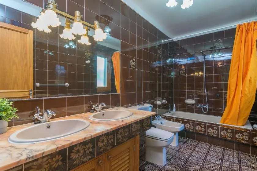Baño alicatado con lavabo doble y una bañera detrás de una cortina naranja.
