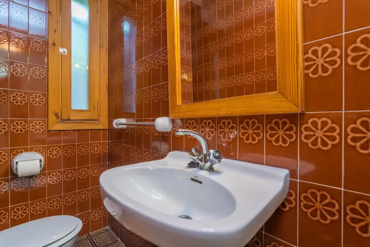 Un baño con un lavabo blanco, paredes de azulejos estampados y una ventana pequeña.