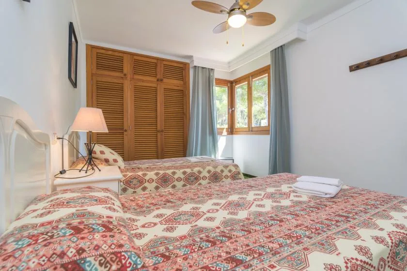 Un dormitorio con ropa de cama estampada, contraventanas de madera y una ventana.