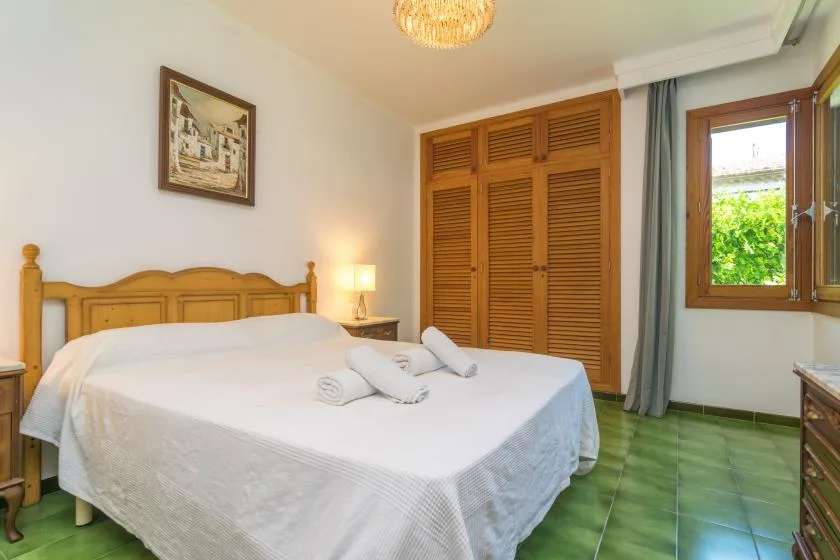 Un dormitorio con una cama de madera, toallas dobladas y una ventana con vistas a la vegetación.
