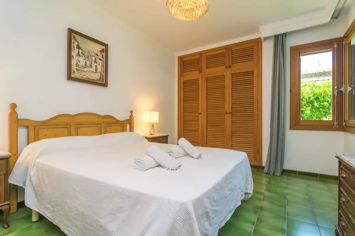 Un dormitorio con una cama doble, armarios con celosías y una ventana con vistas a la vegetación.