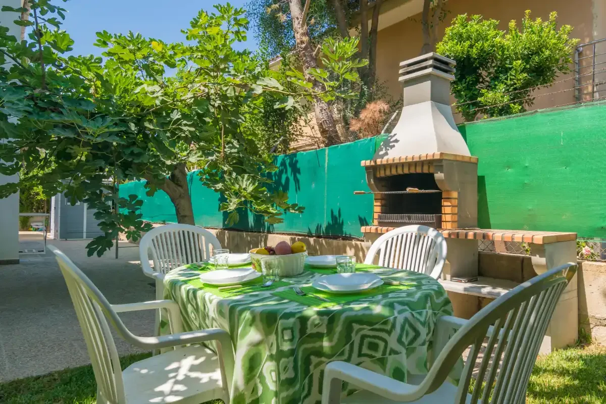 Una zona de comedor exterior a la sombra, con la mesa puesta junto a una barbacoa.