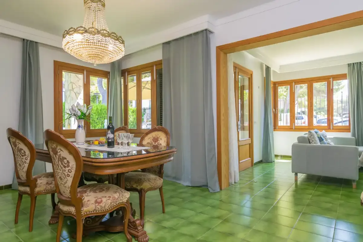 Un comedor se abre a una sala de estar con suelo de baldosas verdes.