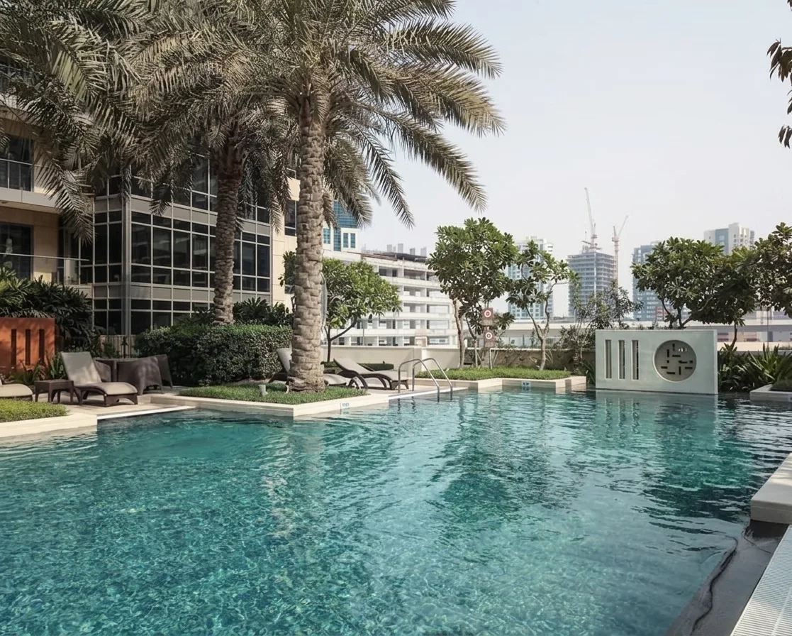 An outdoor swimming pool beside palm trees and modern buildings.