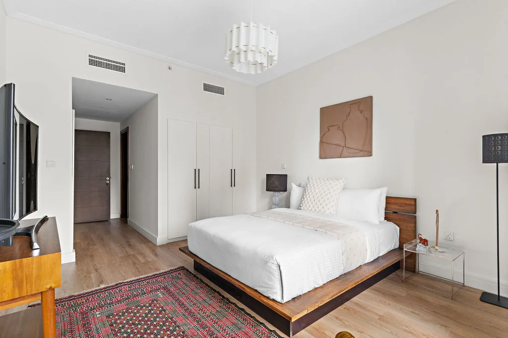 A bright bedroom with a white bed and a small bedside table.