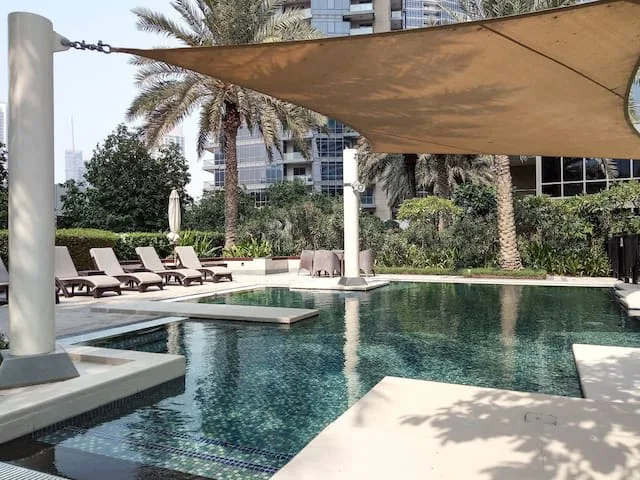 An outdoor swimming pool with shaded lounge seating and palm trees.