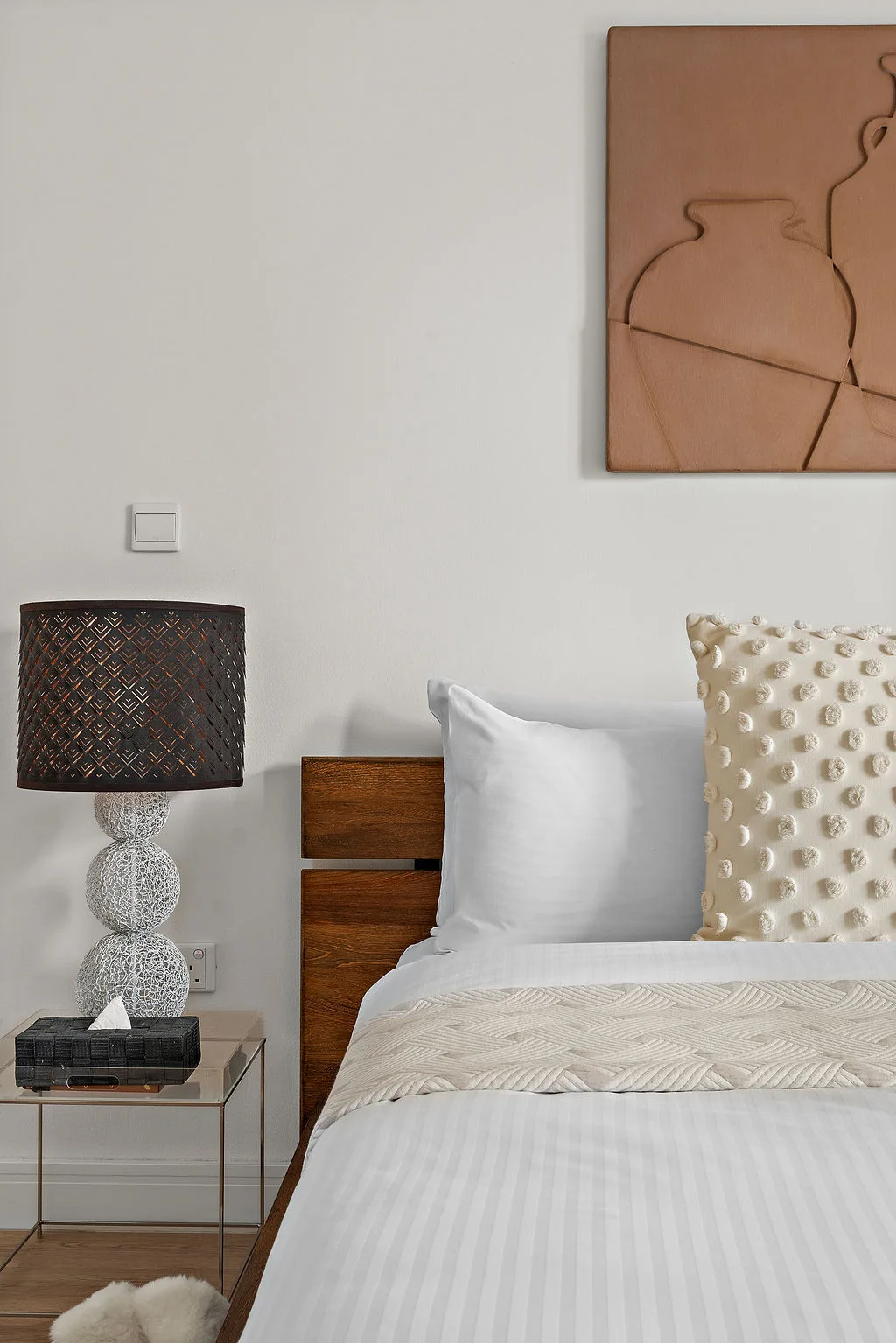 A bedroom with a neatly made bed, bedside table, and lamp.