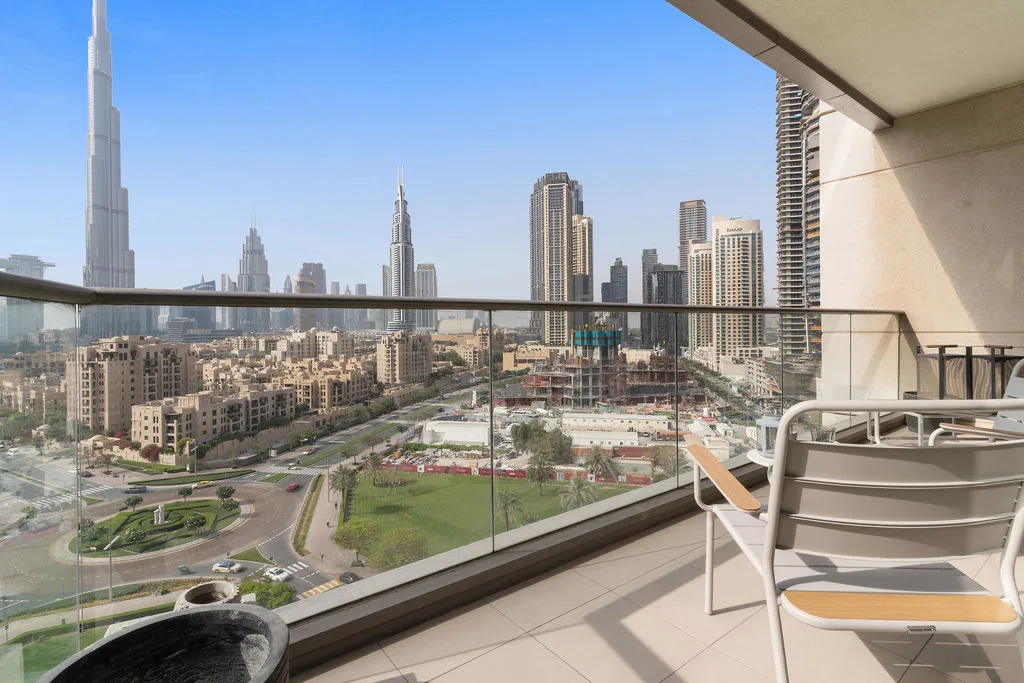 A balcony overlooks a city skyline, with outdoor seating beside the glass railing.