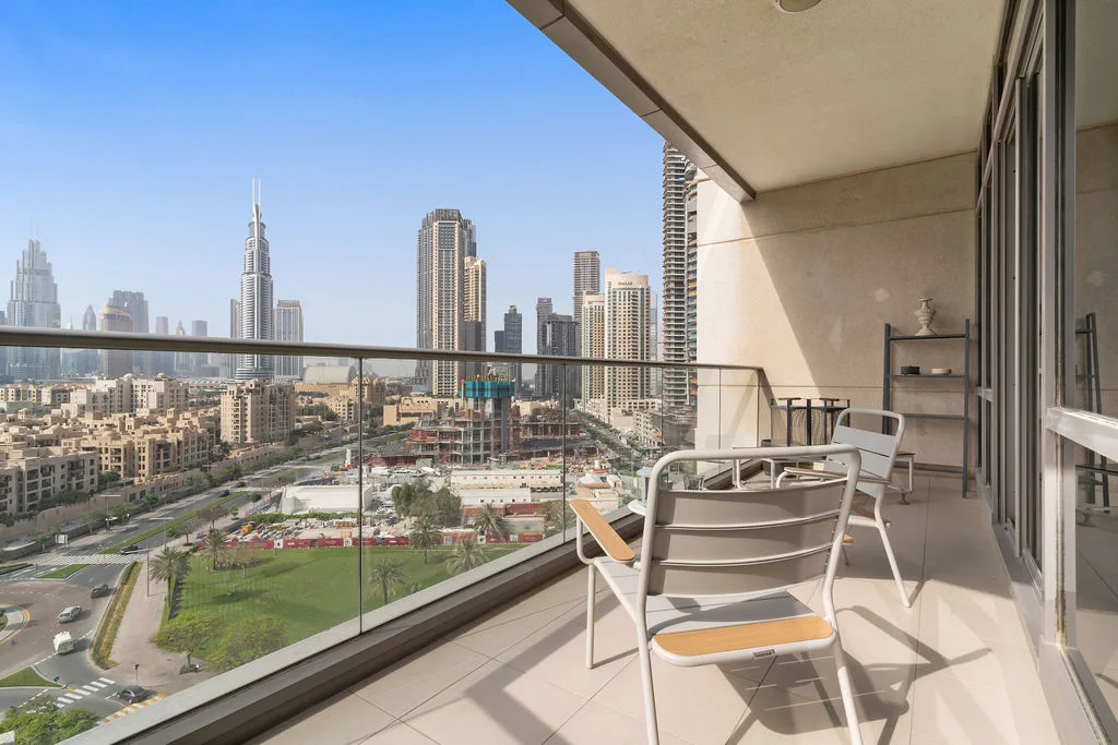 A balcony seating area overlooks a city skyline through a glass railing.