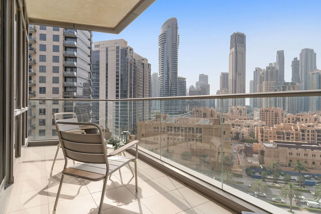 A balcony with outdoor seating overlooks a cluster of high-rise buildings.