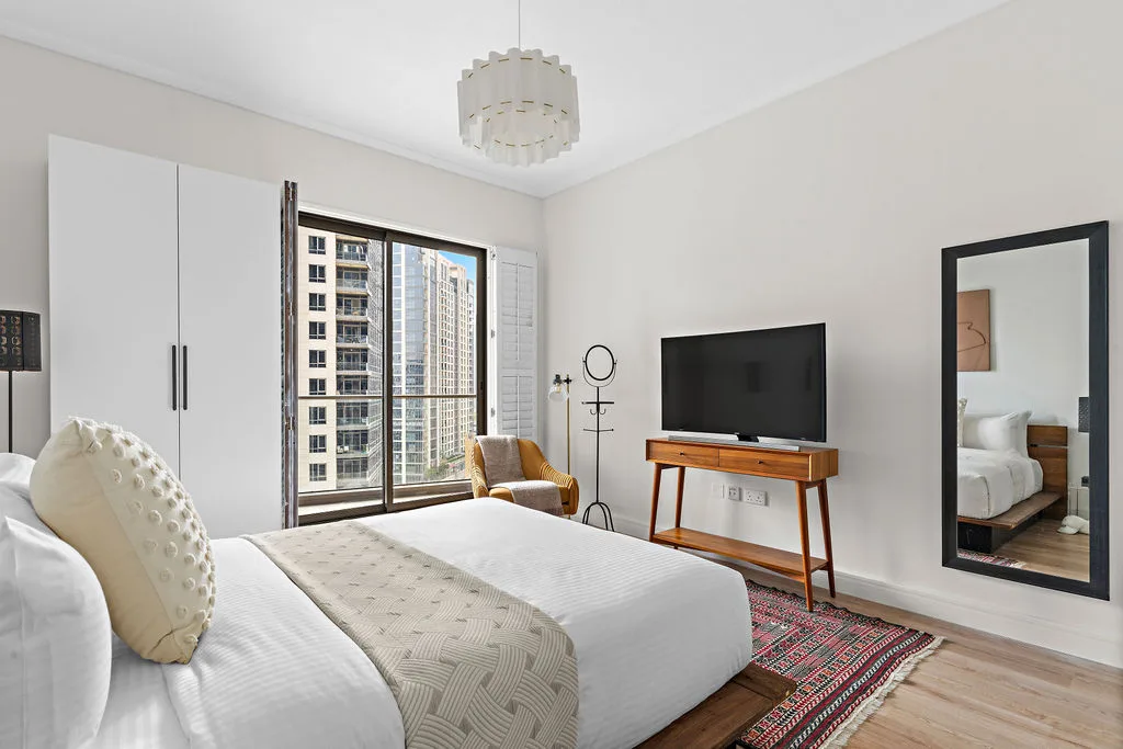 A bright bedroom with a bed, television, and large windows.