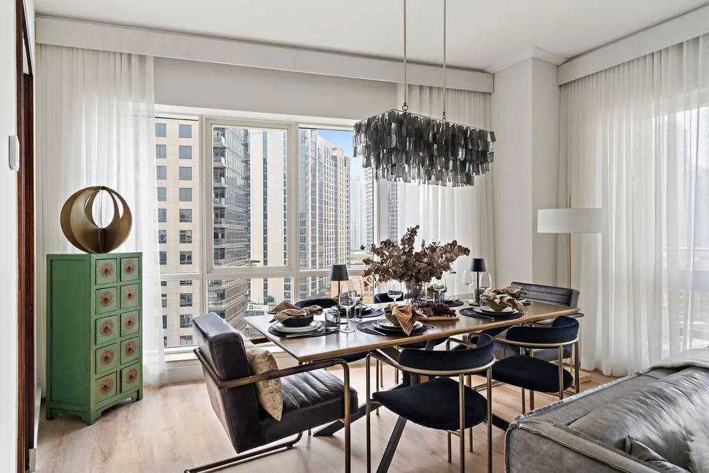 A dining area with a set table beside large windows overlooking nearby buildings.