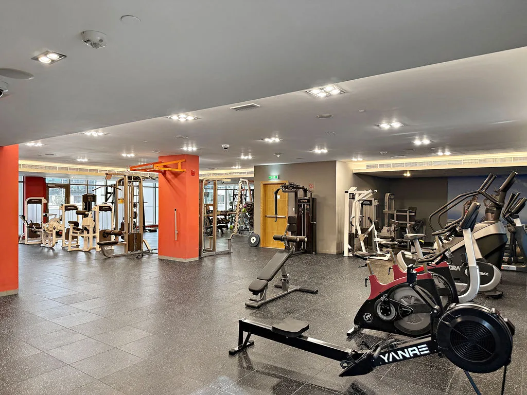 A spacious gym with exercise machines and stationary bikes on a tiled floor.