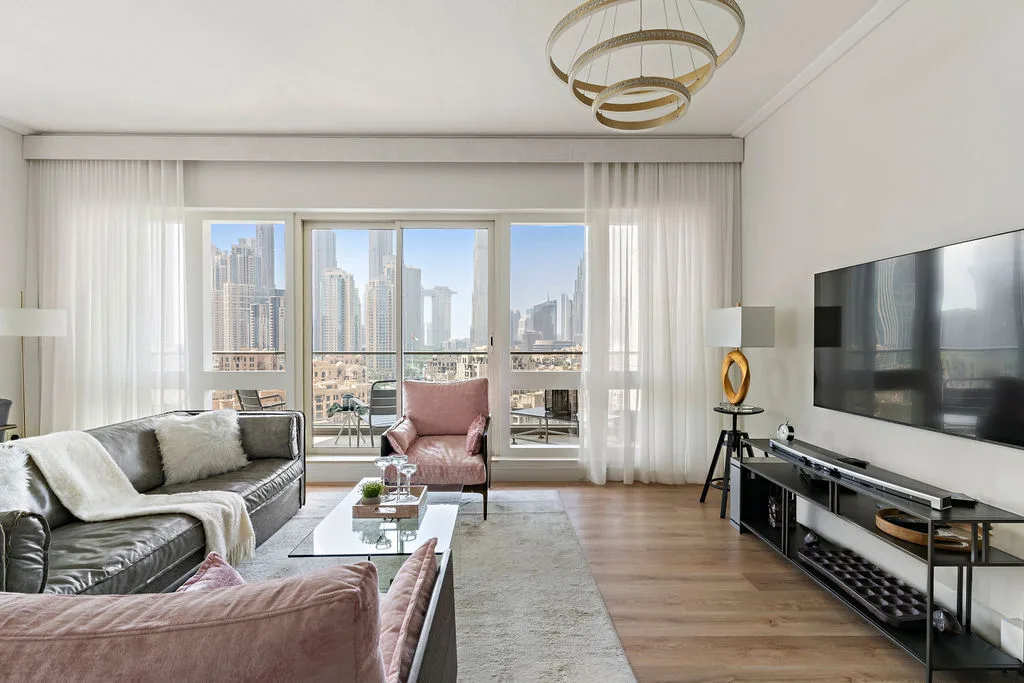 A bright living room with seating, a large television, and windows overlooking city buildings.