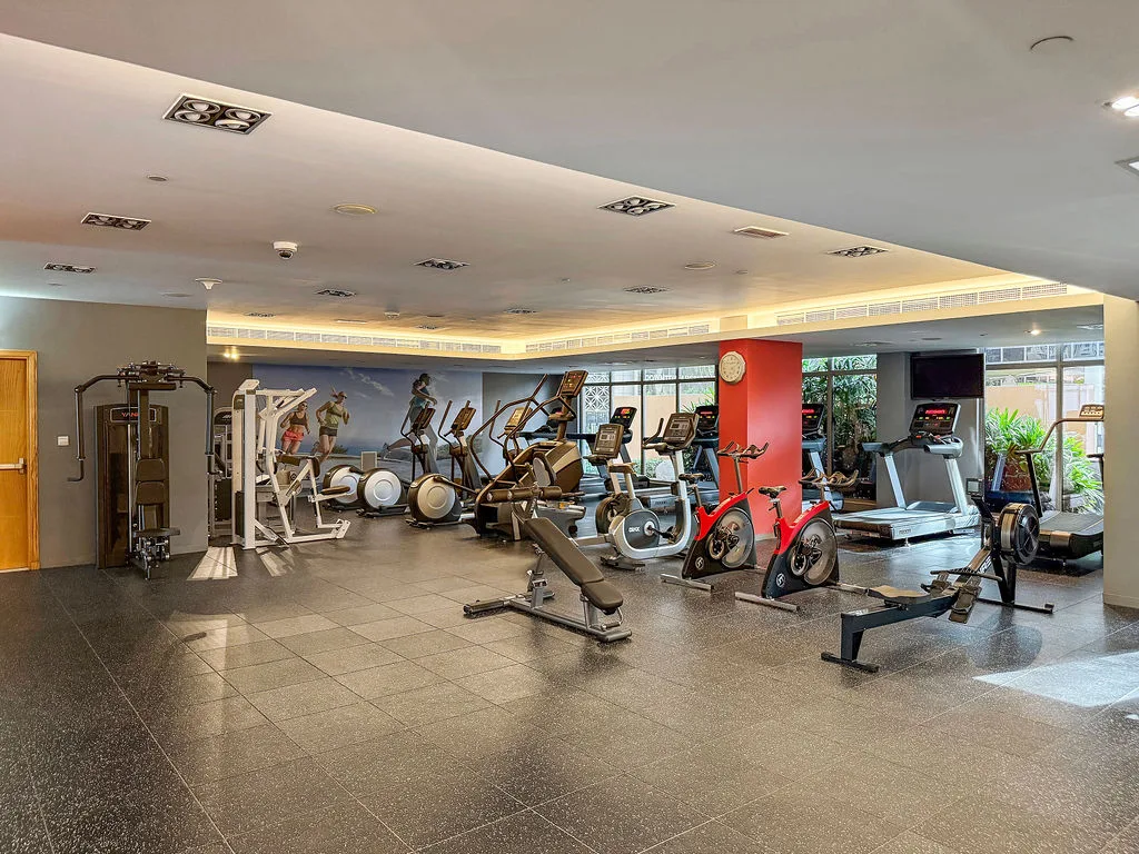 A spacious gym with exercise machines, weight equipment, and large windows.